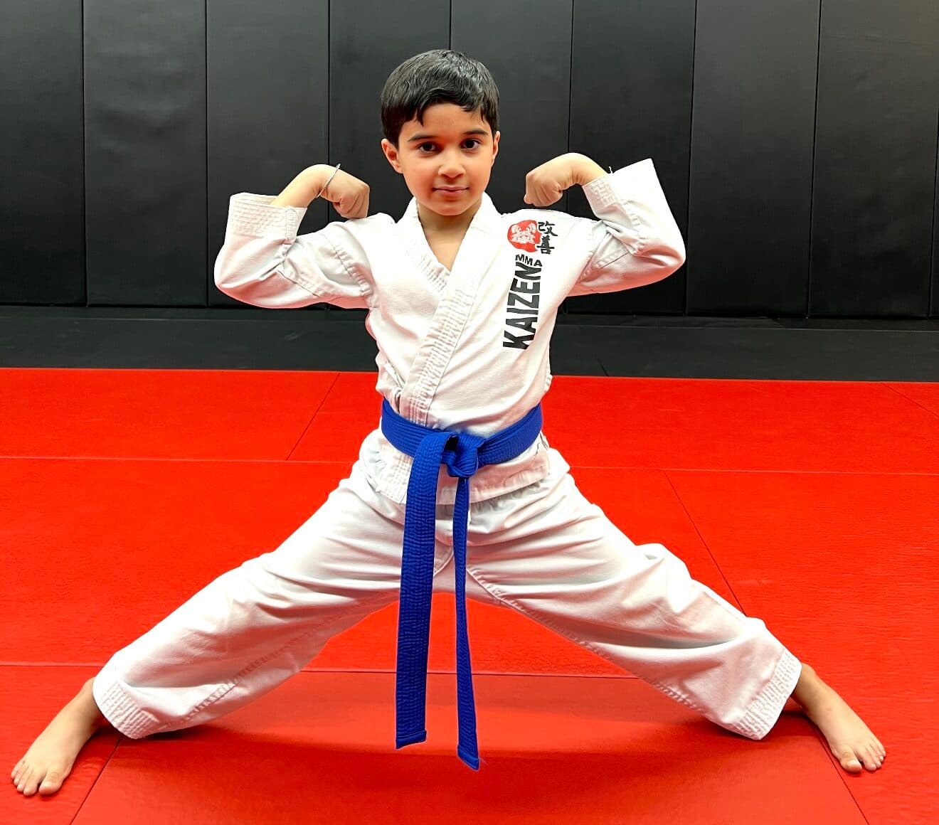 A young Little Lion in a Kaizen gi and blue belt striking a confident pose on the mats at South Riding