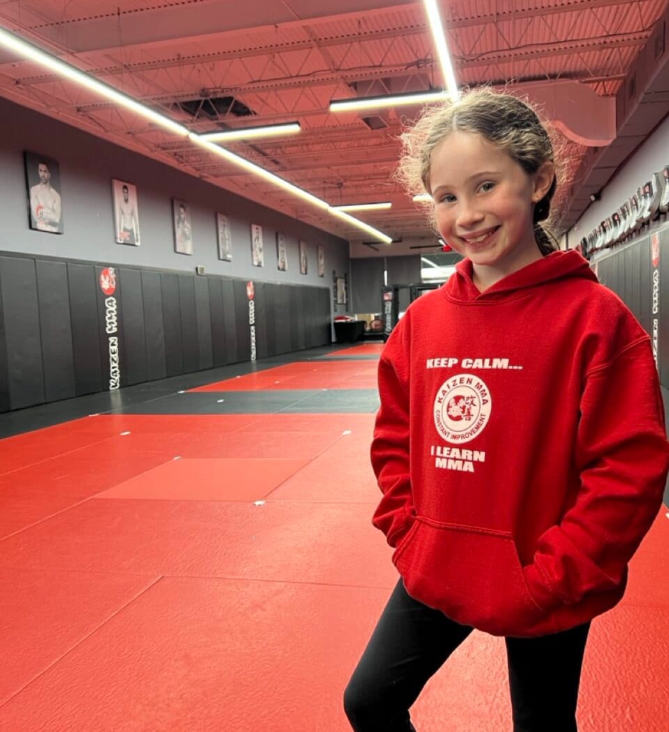 A smiling young student in a Kaizen MMA hoodie on the mats at South Riding