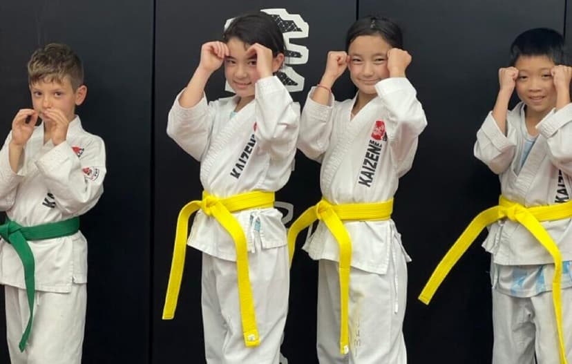 Kids in Kaizen gis with fists up in front of the logo wall at South Riding