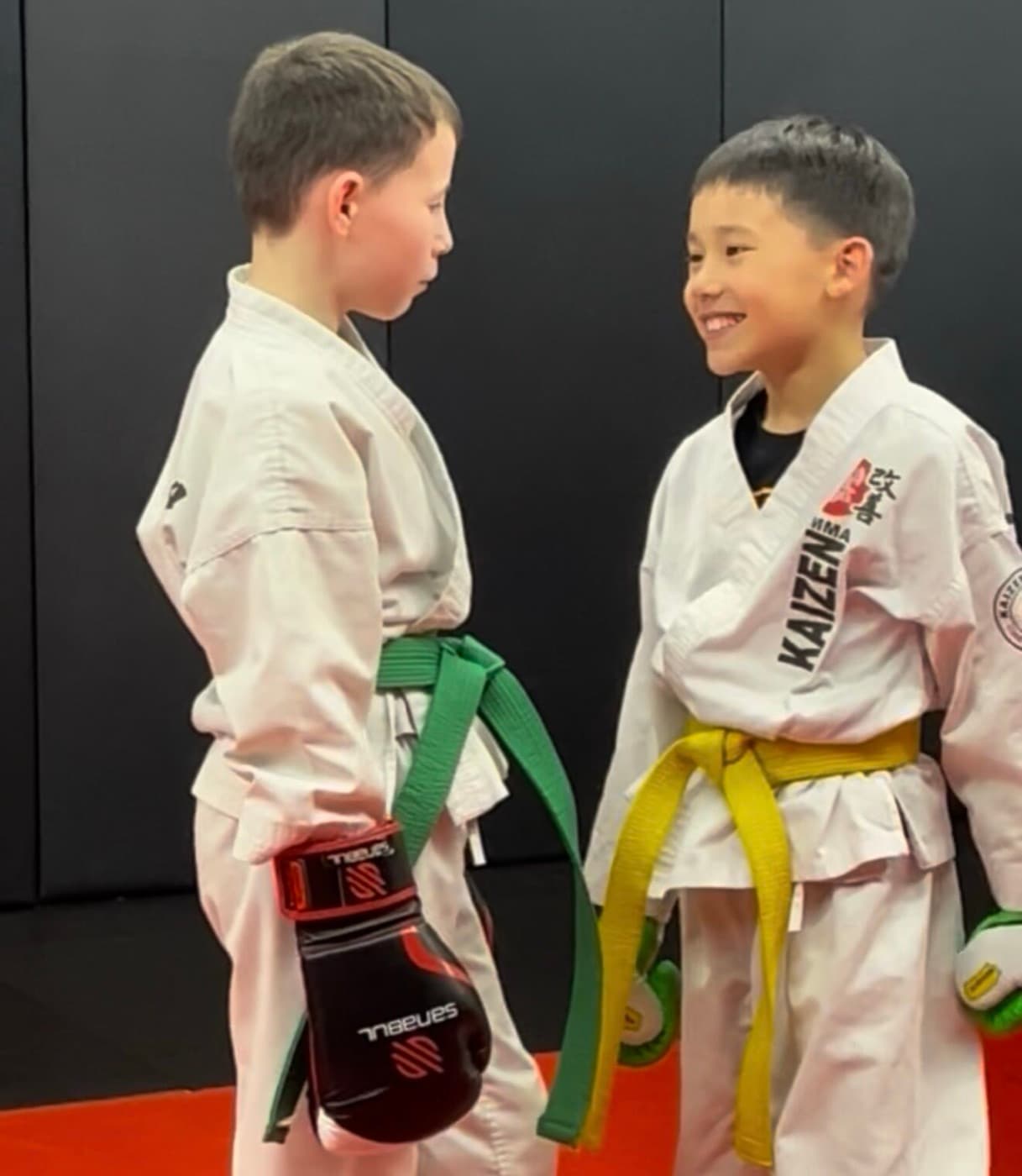 Two Young Lions students in Kaizen gis and sparring gloves sharing a laugh on the mats at South Riding